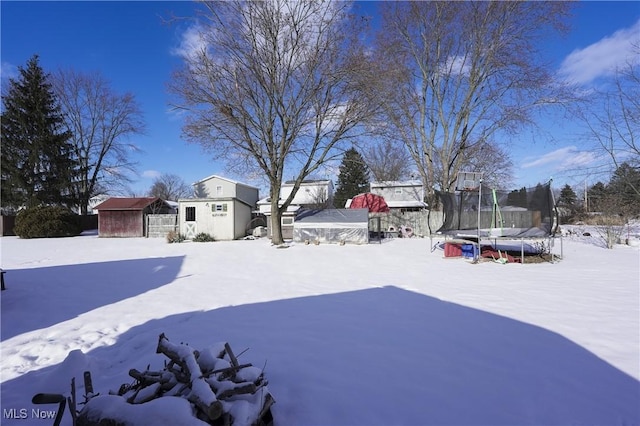 snowy yard featuring a trampoline and a shed