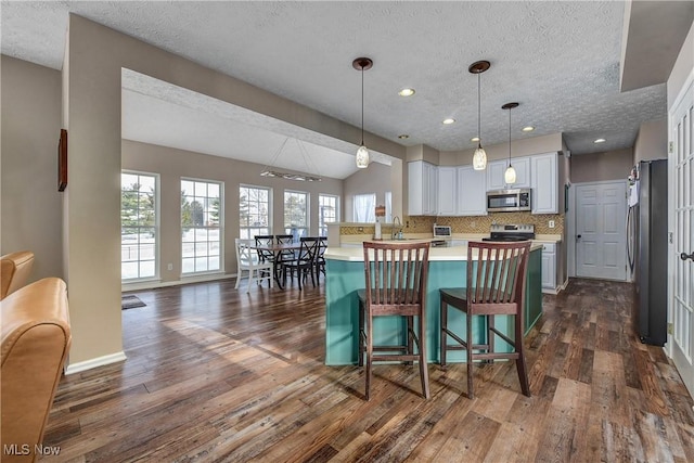 kitchen featuring white cabinetry, a breakfast bar area, decorative backsplash, stainless steel appliances, and a textured ceiling