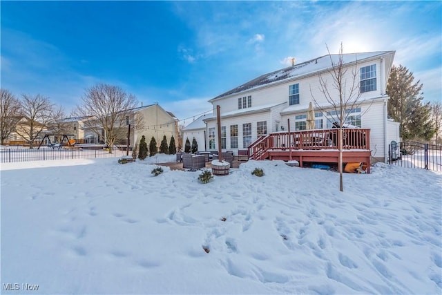 snow covered back of property with a deck and a fire pit