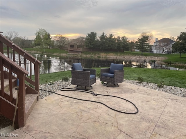 patio terrace at dusk with exterior fireplace, a lawn, and a water view