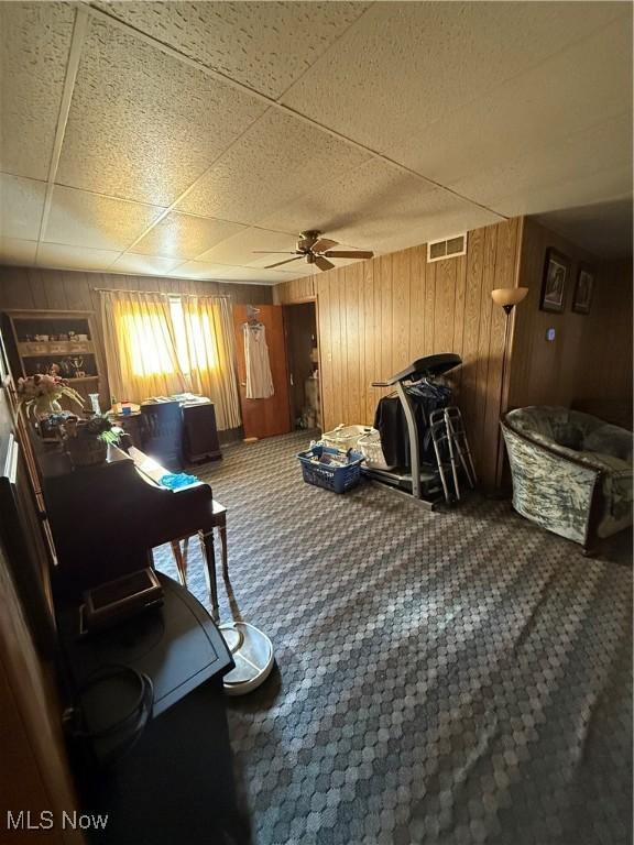 sitting room featuring carpet floors, wooden walls, and ceiling fan