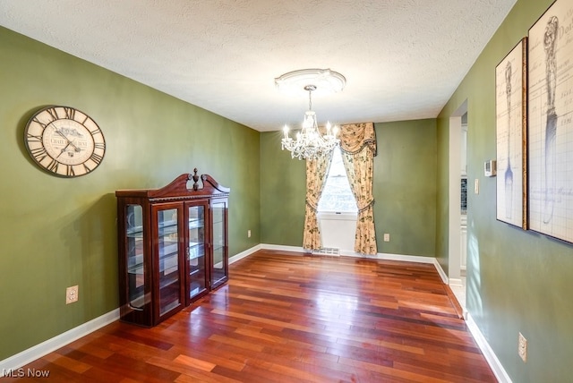 unfurnished dining area featuring dark wood-type flooring, an inviting chandelier, and a textured ceiling