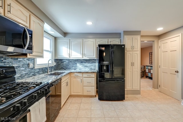 kitchen with sink, light tile patterned floors, backsplash, light stone counters, and black appliances