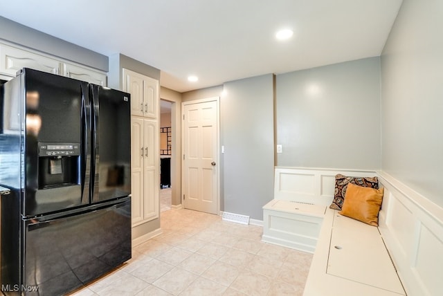 kitchen with light tile patterned floors, white cabinets, and black fridge with ice dispenser