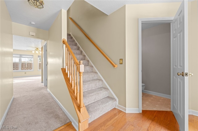 stairs with ceiling fan, hardwood / wood-style floors, and a textured ceiling