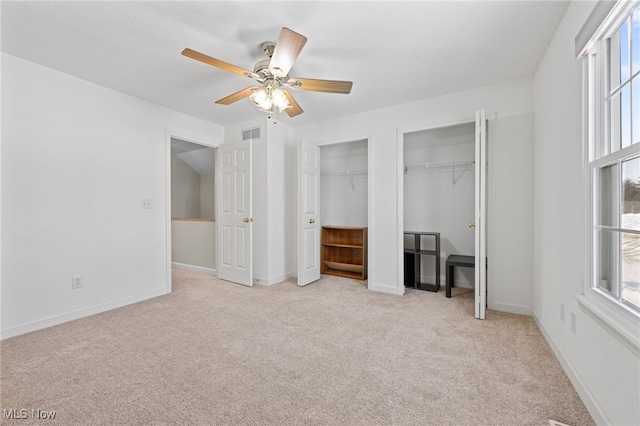 unfurnished bedroom featuring multiple closets, light colored carpet, and ceiling fan