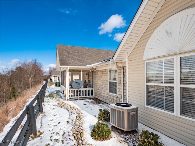 snow covered property with central AC unit and covered porch