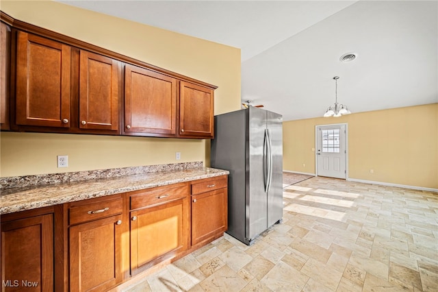 kitchen with lofted ceiling, stainless steel fridge, light stone countertops, decorative light fixtures, and a chandelier