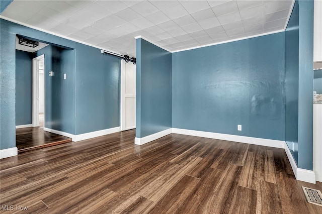 empty room with crown molding, dark wood-type flooring, and a barn door