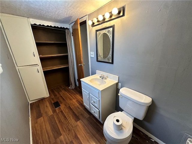 bathroom featuring wood-type flooring, toilet, vanity, and a textured ceiling