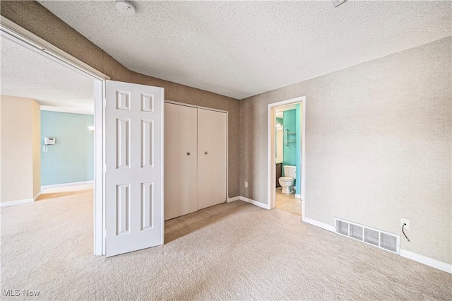 unfurnished bedroom featuring connected bathroom, light colored carpet, a textured ceiling, and a closet