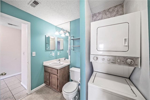 bathroom featuring stacked washer and dryer, vanity, a textured ceiling, tile patterned floors, and toilet