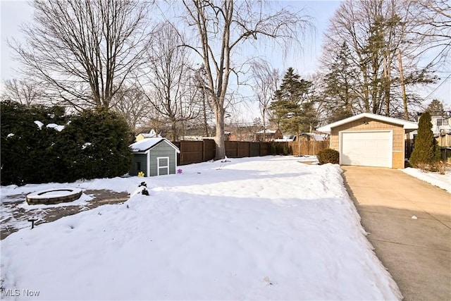 yard covered in snow featuring a storage shed and a garage