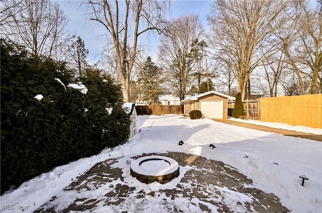 yard covered in snow featuring a garage, an outdoor structure, and an outdoor fire pit