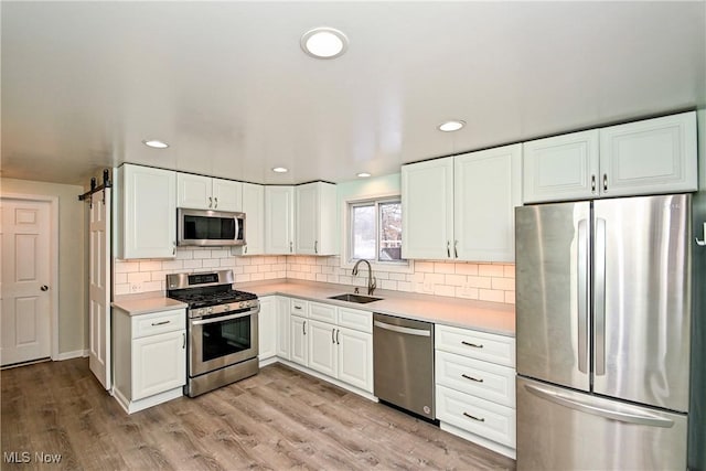 kitchen featuring sink, light hardwood / wood-style flooring, appliances with stainless steel finishes, white cabinets, and backsplash