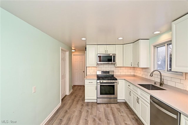 kitchen with white cabinetry, sink, decorative backsplash, stainless steel appliances, and light wood-type flooring