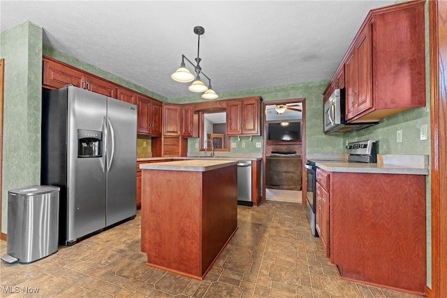 kitchen with sink, ceiling fan, appliances with stainless steel finishes, a center island, and decorative light fixtures