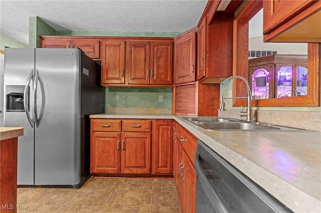 kitchen featuring stainless steel refrigerator with ice dispenser, dishwasher, sink, and a textured ceiling