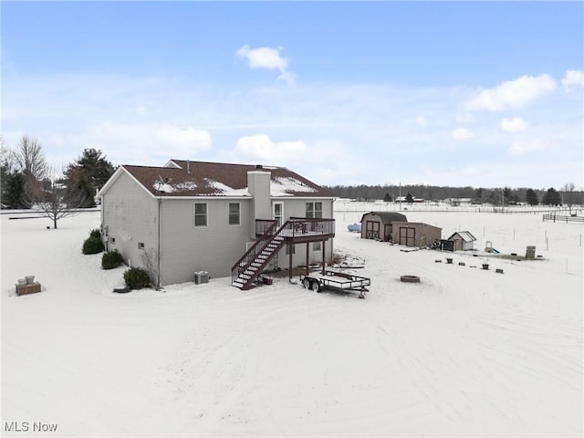 snow covered rear of property with a deck and a storage shed