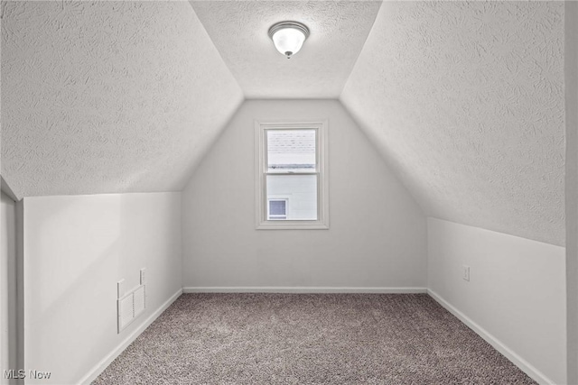 additional living space featuring carpet flooring, vaulted ceiling, and a textured ceiling