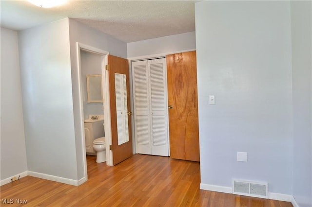 unfurnished bedroom featuring ensuite bath, a textured ceiling, light hardwood / wood-style floors, and a closet