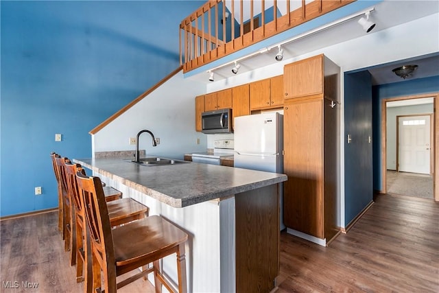 kitchen with sink, white appliances, a breakfast bar, dark hardwood / wood-style floors, and kitchen peninsula