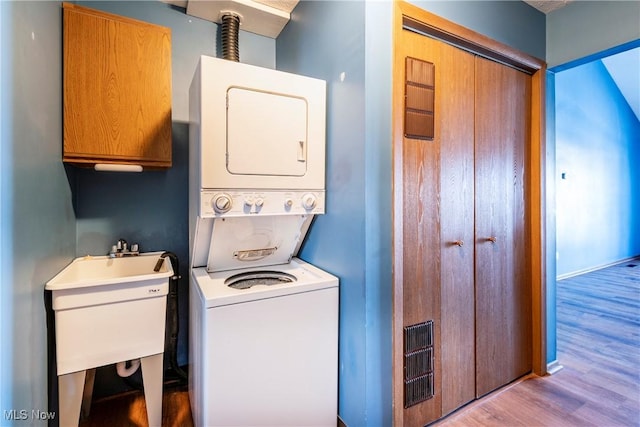 washroom featuring cabinets, stacked washer and clothes dryer, sink, and light wood-type flooring