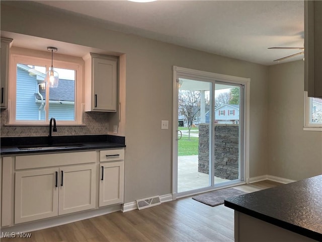 kitchen with sink, white cabinetry, hanging light fixtures, tasteful backsplash, and light hardwood / wood-style floors