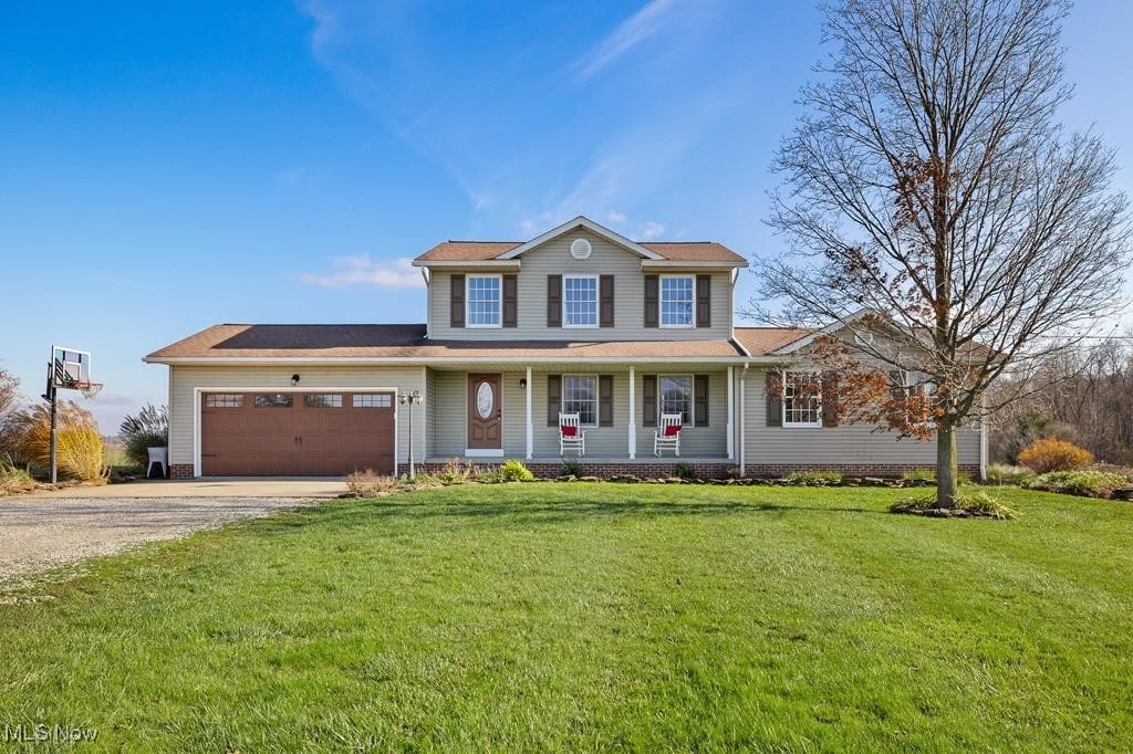 view of front of home with a garage, covered porch, and a front lawn