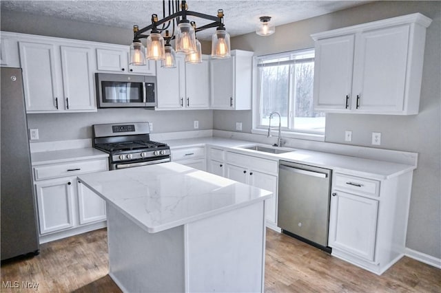 kitchen with appliances with stainless steel finishes, sink, white cabinets, hanging light fixtures, and a center island