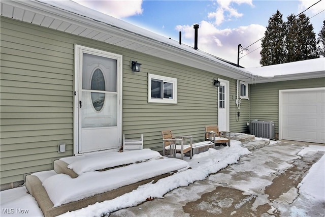 snow covered property entrance with central AC unit and a garage