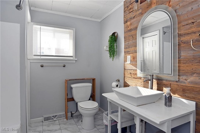 bathroom featuring toilet, ornamental molding, wooden walls, and sink