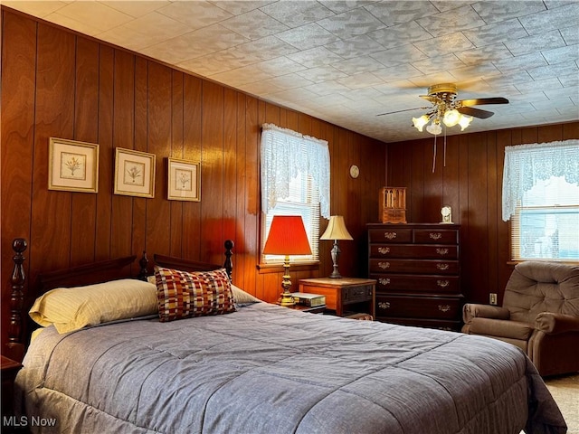 bedroom featuring ceiling fan and wood walls