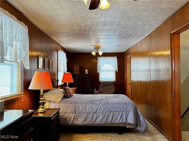 carpeted bedroom featuring ceiling fan and wood walls