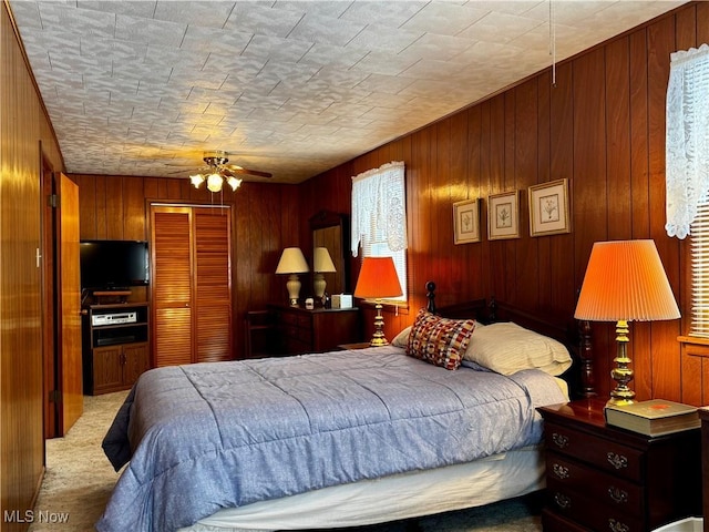 bedroom featuring light carpet, a closet, ceiling fan, and wood walls