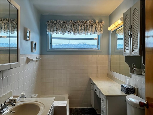 bathroom featuring toilet, vanity, a bath, and tile walls