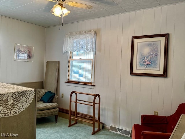 sitting room featuring carpet floors, ceiling fan, and wood walls