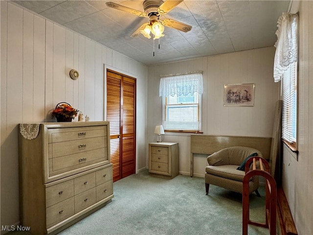 living area featuring light carpet, wooden walls, and ceiling fan