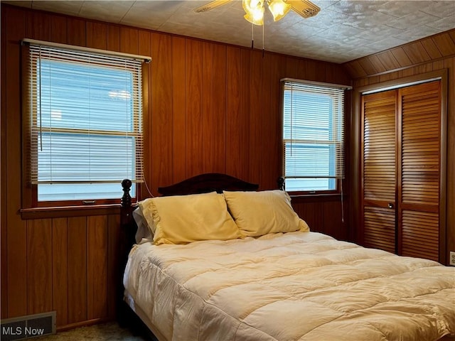 bedroom with carpet flooring, a closet, ceiling fan, and wood walls