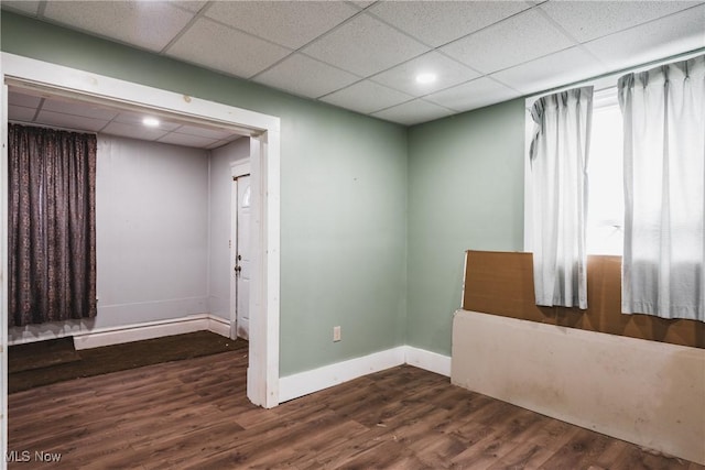 spare room with dark hardwood / wood-style flooring and a drop ceiling