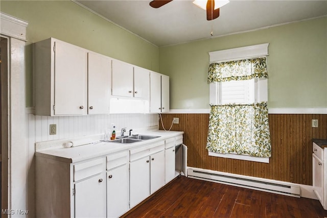 kitchen featuring white cabinetry, a baseboard radiator, sink, and wood walls