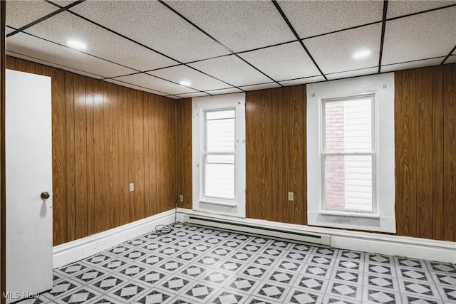 spare room with a baseboard radiator, a paneled ceiling, and wood walls