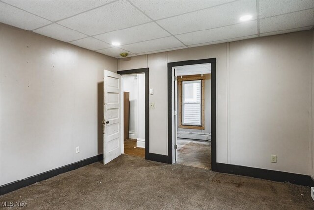 unfurnished bedroom featuring a baseboard heating unit, a drop ceiling, and dark carpet