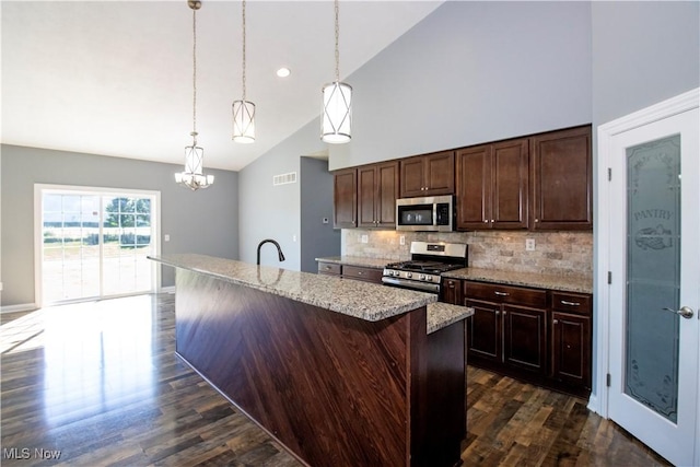 kitchen featuring tasteful backsplash, high vaulted ceiling, hanging light fixtures, a center island with sink, and stainless steel appliances