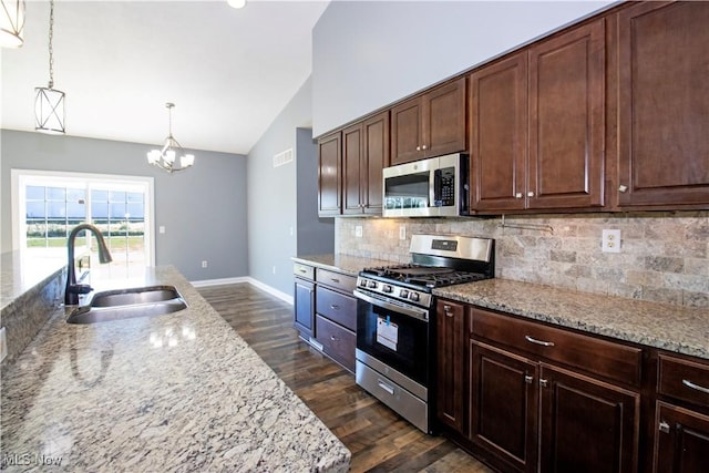 kitchen with appliances with stainless steel finishes, lofted ceiling, sink, hanging light fixtures, and light stone countertops