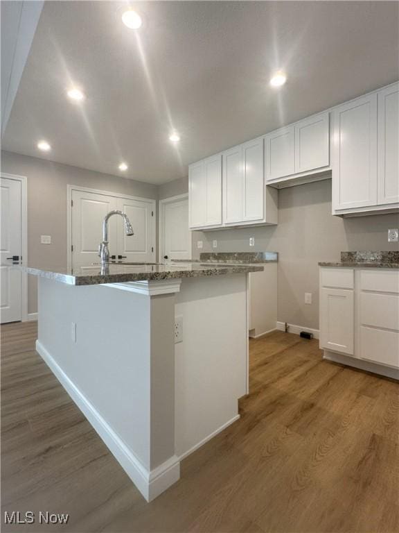 kitchen with stone countertops, a center island with sink, light wood-style flooring, and white cabinets