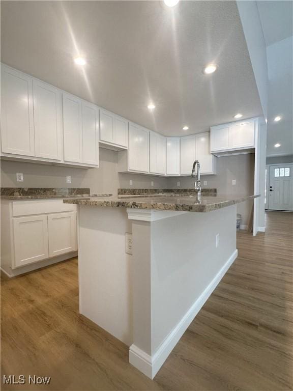 kitchen with dark stone countertops, hardwood / wood-style flooring, an island with sink, and white cabinets