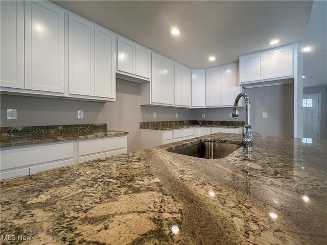 kitchen featuring dark stone counters, sink, and white cabinets