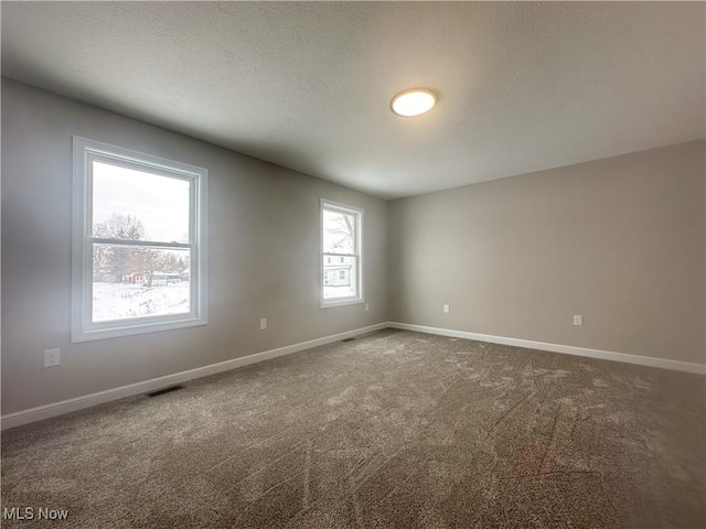 unfurnished room featuring a textured ceiling, dark colored carpet, visible vents, and baseboards