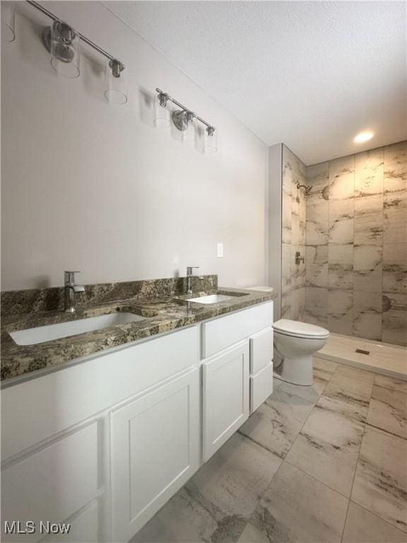 bathroom with marble finish floor, double vanity, toilet, a sink, and tiled shower